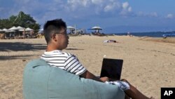 来自成都的阿莫尼奥·梁在巴厘岛海滩上使用笔记本电脑工作。(2023年6月22日)