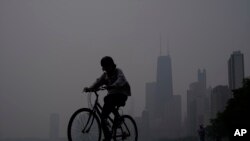 资料照片 - 2023 年 6 月 27 日,伊利诺伊州芝加哥,一名男子沿着密歇根湖岸骑自行车,芝加哥市中心的天际线被加拿大野火的烟雾笼罩。