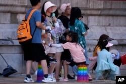 前来北京参观故宫的游客手持小电扇在阴凉地里排队等候入门。(2023年7月7日)