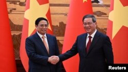 资料照片: 2023年6月26日,越南总理范明政(左)在北京人民大会堂签署仪式后与中国国务院总理李强握手。