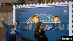 资料照片:2022年10月8日,乌克兰基辅市中心,人们在一张放大的俄罗斯刻赤大桥着火的邮票复制品前自拍。