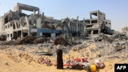 在加沙市西部的斯纳居民区,在以色列军队从该地段撤走后,一名拾捡物件的妇女环视联合国近东巴勒斯坦难民救济和工程处的院落废墟。(2024年7月12日)