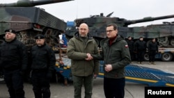 Thủ tướng Ukraine Denys Shmyhal và Thủ tướng Ba Lan Mateusz Morawiecki bắt tay bên cạnh những chiếc xe tăng Leopard 2 đầu tiên được giao từ Ba Lan vào ngày kỉ niệm một năm Nga xâm lược Ukraine, tại một địa điểm không được tiết lộ, Ukraine, ngày 24 tháng 2 năm 2023.