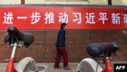 资料照:一名妇女走过北京街头宣传习近平新时代的标语。(2017年10月27日)