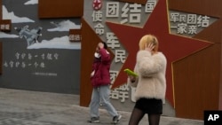 两个年轻人走过北京街头一堵政府的宣传墙。(2024年1月17日)