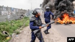 2023 年 12 月 27 日,金沙萨反对派示威期间,刚果民主共和国警察站在燃烧的路障旁。