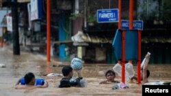 在菲律宾大马尼拉马里基纳市,居民在台风“格美”带来的暴雨后涉水通过被洪水淹没的道路。(2024年7月24日)