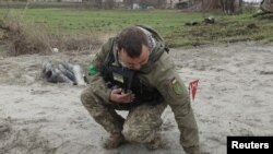 资料照片:2022 年 4 月 10 日,一名工兵在俄罗斯入侵乌克兰基辅地区某村附近捡起一枚集束炸弹的未爆炸部分。(路透社照片)