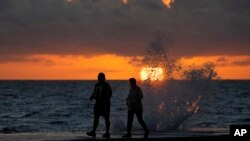 2022年12月7日,佛罗里达州巴尔港,随着海浪拍打海滩游客附近的码头,太阳从大西洋升起。