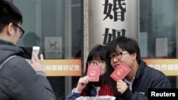 资料照:一对年轻人在北京一个婚姻登记处外手举结婚证留影。(2017年2月14日)