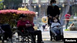 在上海一个公园里,一名女子推着小女孩路过一位坐轮椅的老人。(2023年4月2日)