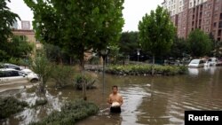 资料照:河北涿州一名男子手拿食物走在积满洪水的街道上。(2023年8月3日)