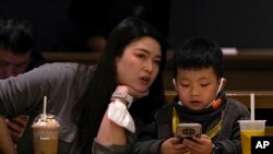 资料照 - 2023年1月19日北京一座咖啡馆里,一位母亲正在和她孩子说话,而儿子却目不转睛地玩着手上的智能手机。