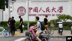 北京街头人们路过中国人民大学校园外墙的标识。(2024年7月22日)