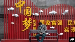 资料照:一名戴着口罩的男子在武汉街头一个中国梦的政府宣传牌下打盹。(2020年4月8日)