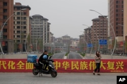 中国河北雄安街头一名快递小哥在口号横幅前休息。(2023年4月1日)