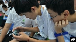 资料照片:2023年8月17日,在北京举行的年度世界机器人大会上,一名学生帮助他的同学通过智能手机玩网络游戏。(美联社照片)