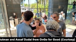 幸存者在人群中举着手机中失踪的亲人的照片。(照片受访者提供)