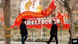 资料照:新疆和田居民走过街头竖立的社会主义核心价值观的宣传牌。(2021年3月22日)