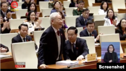 Ảnh chụp màn hình buổi tường thuật trực tiếp của Quốc hội TV vào lúc 8:02 phút ngày 15/1 năm 2024 cho thấy ông Trọng đang đứng lên một cách khó nhọc khi được xướng tên