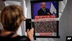 以色列特拉维夫的一名女子用手机拍摄的一张海报照片显示，内塔尼亚胡总理照片下贴有被关押在加沙的以色列人质的照片，海报要求以色列领导人达成协议将人质带回家。（2023年11月21日）