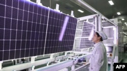 资料照片:2024年1月4日,中国江苏省连云港的一家工厂的一名员工站在将要出口的太阳能光伏组件前。(法新社照片)