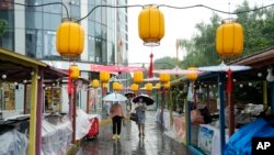 北京居民走过一家因大雨而暂停营业的露天市场。中国央行为提振经济调低了主要利率,为习近平争取第三期连任住一臂之力。
