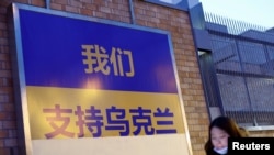 2022年3月2日,在俄罗斯入侵乌克兰后,在加拿大驻北京大使馆外面,一名女子手持手机走过一个支持乌克兰的广告牌。(路透社)