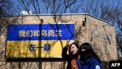 资料照:2022年3月3日,加拿大驻北京大使馆外,人们走过印有“我们和乌克兰在一起”字样的根据乌克兰国旗设计的标牌(法新社)。