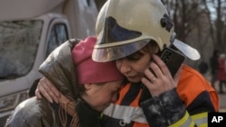 基辅一座居民楼遭轰炸被毁后,消防队员在楼外安慰一名女子。(2022年3月15日)