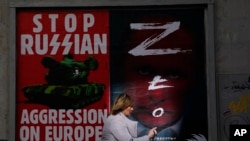 A woman walks past a wall with posters depicting Russian President Vladimir Putin, right, in Warsaw, Poland, March 24, 2022.