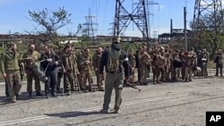 俄罗斯国防部发布的视频截图显示,乌克兰军人从马里乌波尔亚速钢铁厂走出投降,在俄罗斯士兵前站成一排。(2022年5月18日)