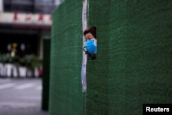 一位上海居民从封闭小区的围栏空隙中伸出头来张望。(2022年5月6日)