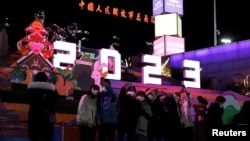 新年前夜,人们站在北京一座大型商场外“2023”字样的灯饰下,而此时新冠病毒正如潮水般在北京卷土重来。霓虹灯庆祝2023年广告背后远处是“中国人民解放军总医院”大楼。