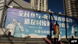 一名女子走过北京街头一幅抗疫宣传画。(2022年12月11日)