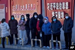 北京市民在宣传习近平思想的标语墙前排队等候接受核酸检测。(2022年12月5日)