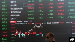 资料照 - 2020年2月14日,一位戴着口罩的男子走过上海股票交易大楼前显示股票走势的巨大电子屏幕。