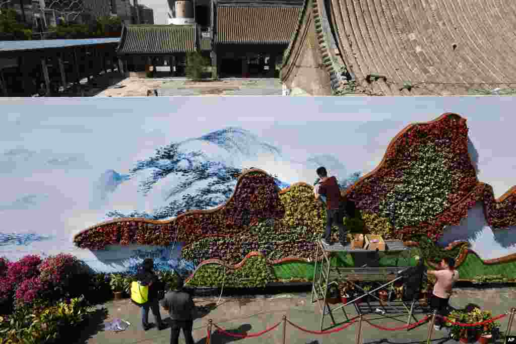 在北京的 “一带一路”国际合作高峰论坛开幕前,在西单文化广场的被部分拆毁的院子周围的围板上,工人们用花铺设山的形状(2017年5月10日)