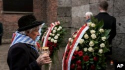 2025年1月27日,在波兰奥斯威辛-比克瑙集中营解放80周年纪念仪式上,一名幸存者拿着蜡烛走向“死亡墙”。