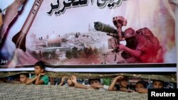 Các thiếu niên Palestine đứng dưới một tấm áp phích lớn của Hamas, để xem cuộc mít-tinh ủng hộ các phe phái vũ trang Palestine, ở Rafah, miền nam Dải Gaza, 17/8/14.