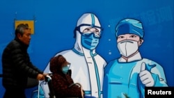 一名男子推着一位坐轮椅的妇女走过北京街头的一堵抗疫宣传墙。(2022年10月27日)