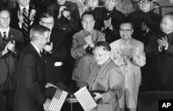 1979年8月28日,美国副总统蒙代尔和中国副总理邓小平在两国文化和水电协议书签署后,交换协议文本。前排鼓掌者有中国总理华国锋(中)、美国驻华大使伦纳德•伍德科克(华国锋左侧)和中国外交部长黄华(华国锋右侧)