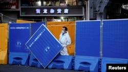 上海一名身穿防护服的工作人员站在封城使用的围栏旁。(2022年4月11日)