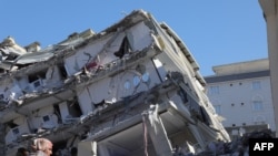 资料照 - 在遭受地震损害严重地区之一的加济安泰普,一位妇女站在一幢倒塌的楼房前。