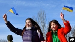 两位女士在乌克兰的克拉马托尔斯克举着乌克兰国旗,度过“团结日”。(2022年2月16日)