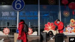 旅客戴着口罩拖着行李来到北京首都机场国际航班出发航站楼入口(2022年12月29日)