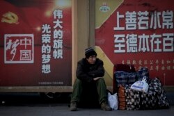 一名民工坐在北京火车站外树立的中国政府的宣传牌下。(2019年1月21日)
