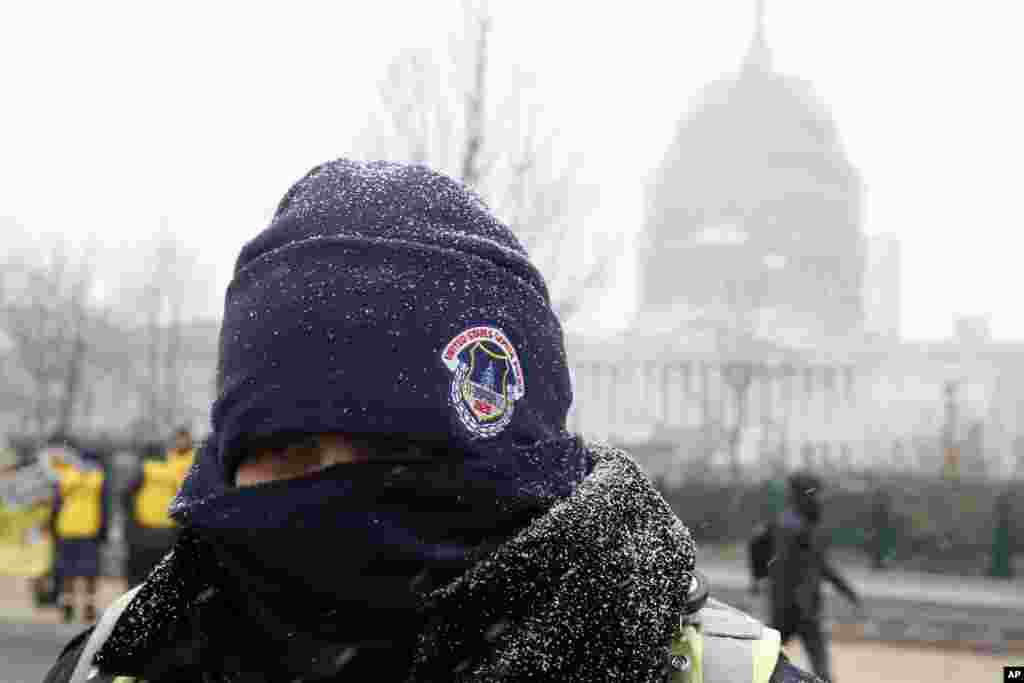 Snow begins to stick on the cap and jacket of a U.S. Capitol Police, in front of the U.S. Capitol in Washington D. C., Jan. 22, 2016.