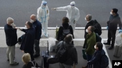 世卫组织的专家们抵达武汉天河国际机场,身穿防护服的中国工作人员给他们指方向。(2021年1月14日)