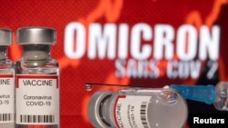 资料图:在写有“奥密克戎SARS-COV-2”背景前,放置着标识为“COVID-19冠状病毒”的疫苗瓶和注射器。